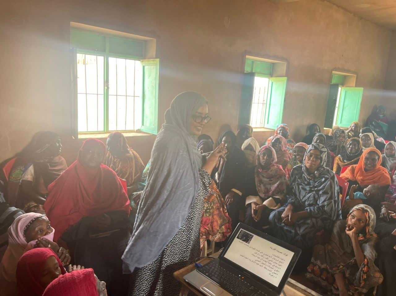Dr. Nada Alassad gestures while explaining a point to seated women; sunlight streams through the windows behind her.